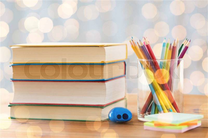 Education, school, creativity and object concept - close up of crayons or color pencils with books, stickers and sharpener on wooden table over holidays lights background, stock photo