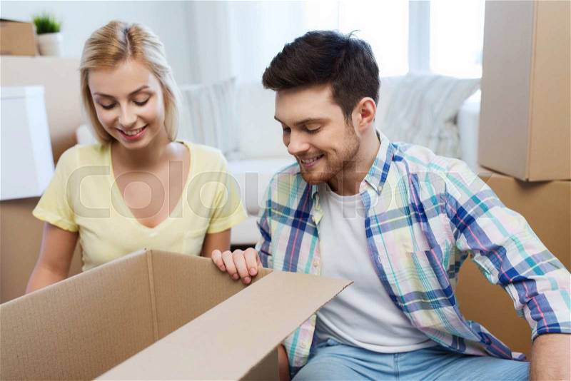 Moving, people, repair and real estate concept - smiling couple looking into big cardboard box at new home, stock photo