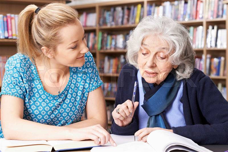 Senior Woman Working With Teacher In Library, stock photo