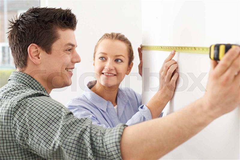 Young Couple Measuring Wall In New Home, stock photo