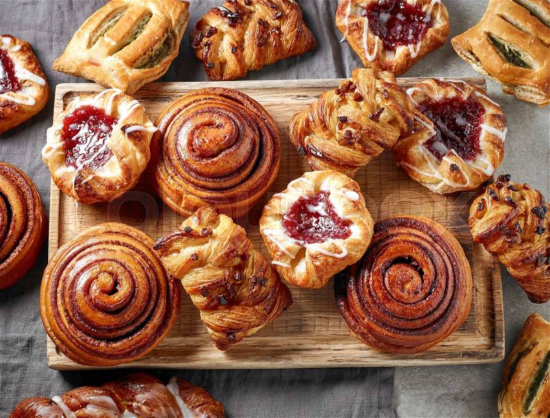 Various freshly baked sweet buns on wooden cutting board, top view, stock photo