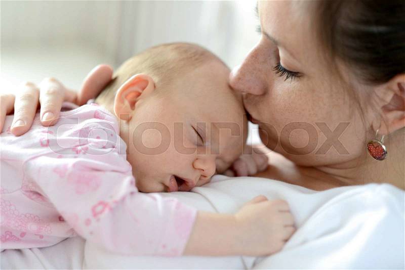 Close up of young mother holding her cute baby daughter lying on her, sleeping, kissing her, stock photo
