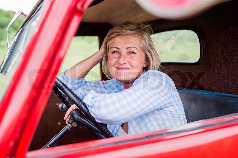 Close up of senior woman in checked blue shirt inside vintage pickup truck, stock photo