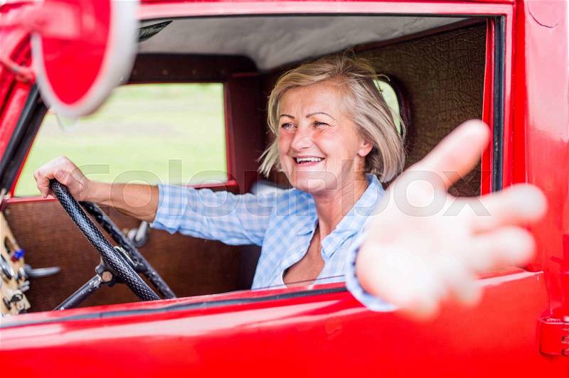 Close up of senior woman in checked blue shirt inside vintage pickup truck, stock photo