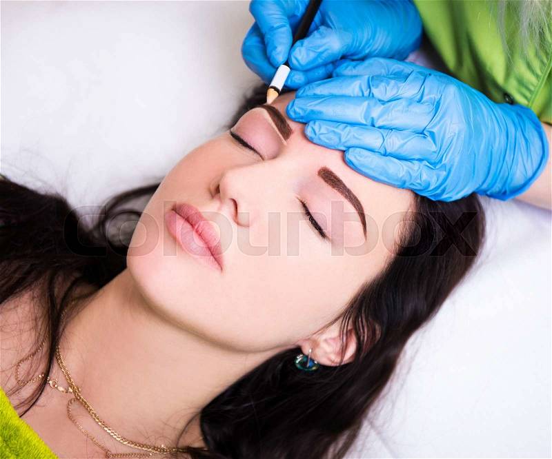Permanent eyebrow make up - close up of beautician preparing woman for procedure, stock photo