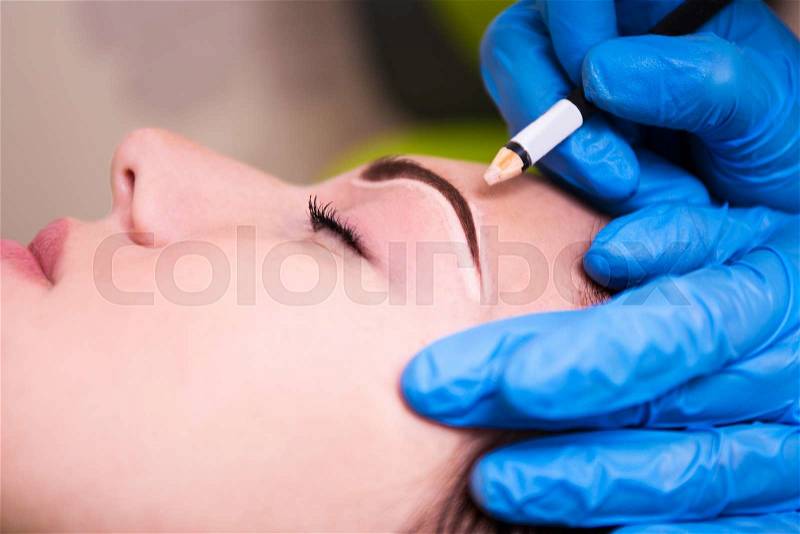 Close up of beautician preparing young beautiful woman for permanent eyebrow make up procedure, stock photo