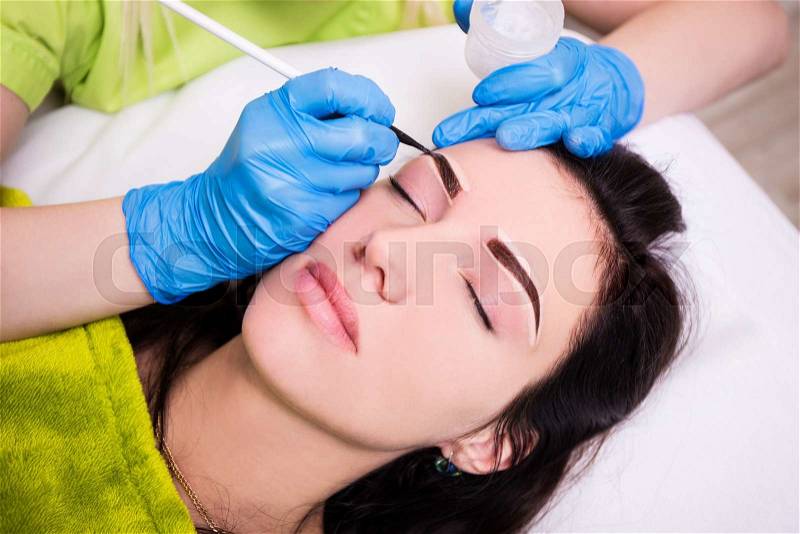 Permanent eyebrow make up - beautician applying anesthesia and preparing young woman for procedure, stock photo