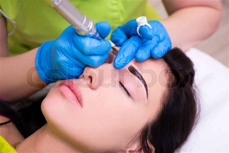 Close up of cosmetologist applying permanent make up on female eyebrows, stock photo