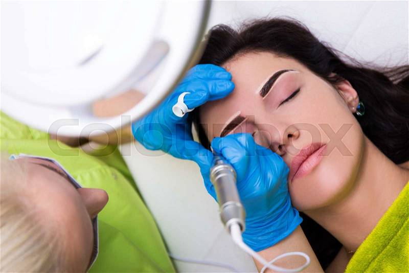 Top view of cosmetologist applying permanent make up on female eyebrows, stock photo