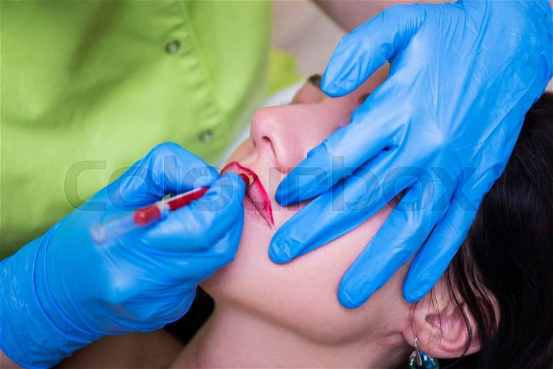 Cosmetician preparing young woman for permanent lips make up, stock photo