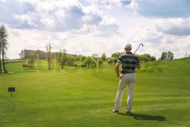 Male golfer standing at fairway on golf course, back view, stock photo