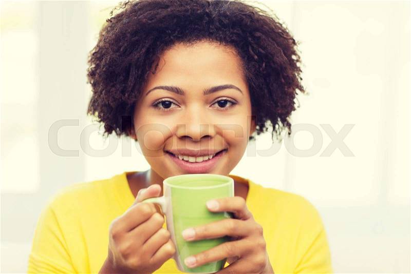 People, drinks and leisure concept - happy african american woman drinking tea from cup or mug at home, stock photo