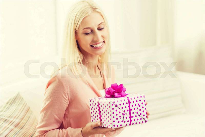 People, holidays, celebration and birthday concept - smiling young woman with gift box at home, stock photo