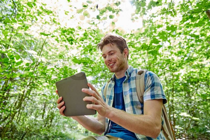 Adventure, travel, tourism, hike and people concept - happy young man with backpack and tablet pc computer in woods, stock photo