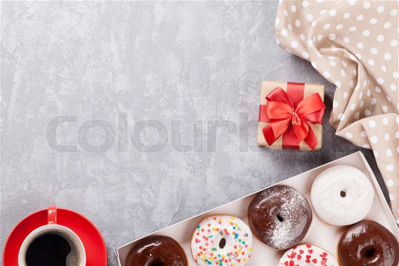 Colorful donuts, gift box and coffee on stone table. Top view with copy space, stock photo
