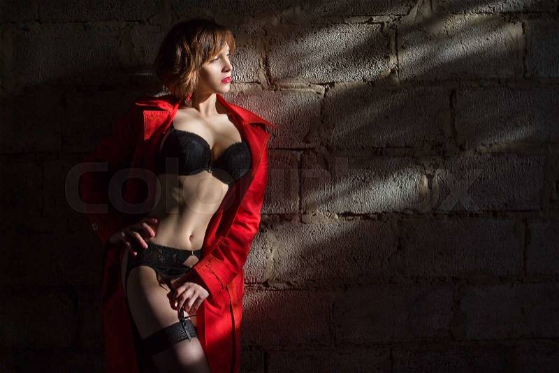 Attractive young woman alluring in sexual lingerie and red coat at grunge industrial setting. Beauty, fashion. Concept: seduction, exhibitionism, stock photo