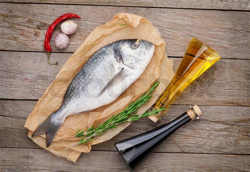 Fresh dorado fish cooking with spices and condiments on wooden table, stock photo