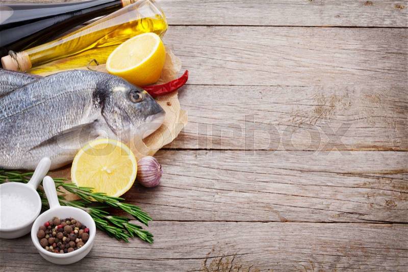 Fresh dorado fish cooking with spices and condiments on wooden table with copy space, stock photo
