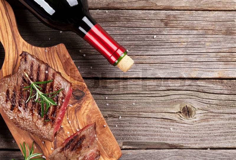 Grilled beef steak with rosemary, salt and pepper and red wine on wooden table. Top view with copy space, stock photo
