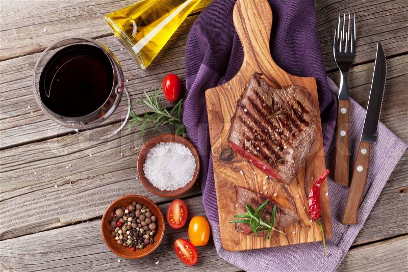 Grilled beef steak with rosemary, salt and pepper and red wine on wooden table. Top view, stock photo