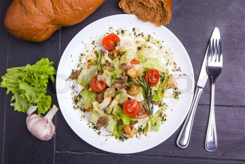 Concept: healthy food. Homemade salad with beef mushrooms and vegetables on white plate with ingredients bread and cutlery around, stock photo