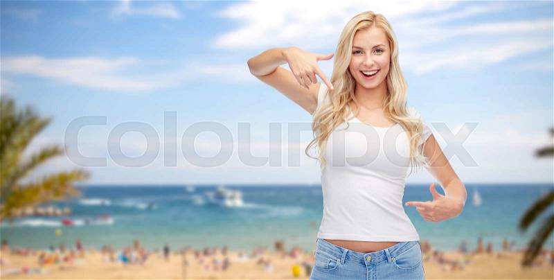 Advertisement, summer holidays, travel and people concept - happy smiling young woman or teenage girl in white t-shirt pointing finger to herself over exotic tropical beach and sea background, stock photo