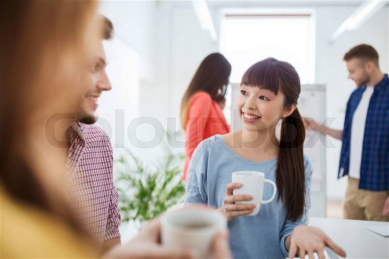 Business, startup and people concept - happy creative team or students drinking coffee and talking at office, stock photo