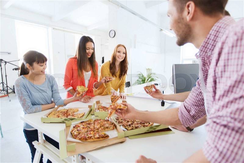 Business, food, lunch and people concept - happy international business team eating pizza in office, stock photo