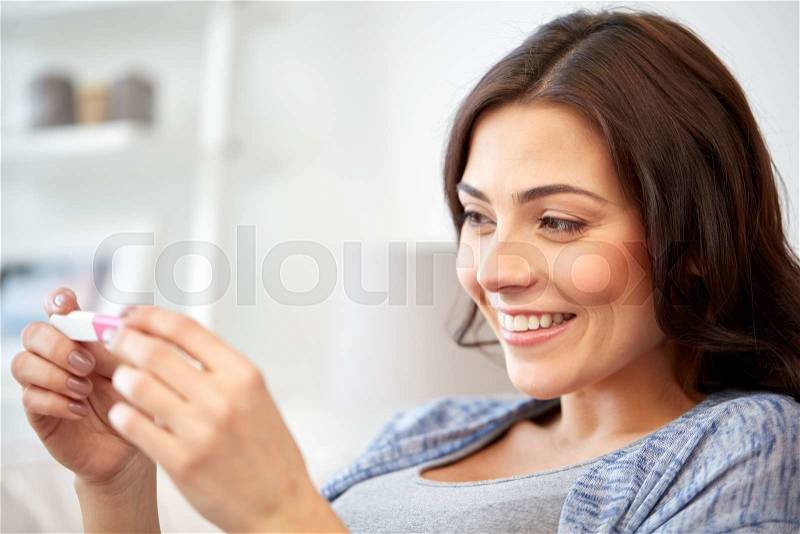 Pregnancy, fertility, maternity and people concept - happy smiling woman looking at pregnancy test at home, stock photo