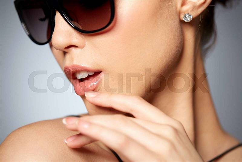 Accessories, eyewear, fashion, people and luxury concept - close up of beautiful young woman in elegant black sunglasses over gray background, stock photo