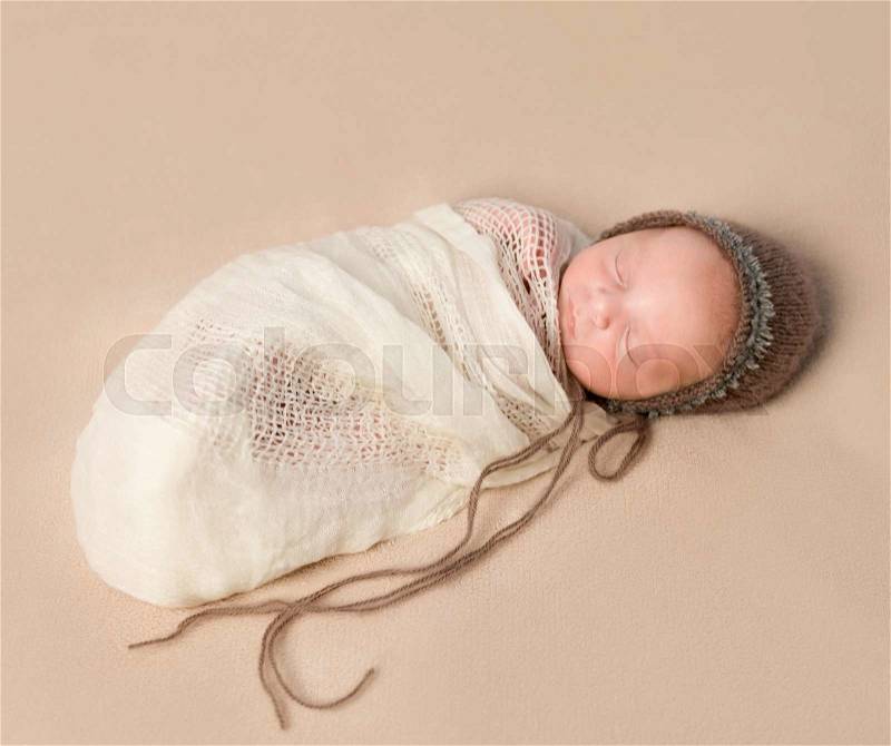 Beautiful sleepy swaddled newborn baby in knitted hat , stock photo