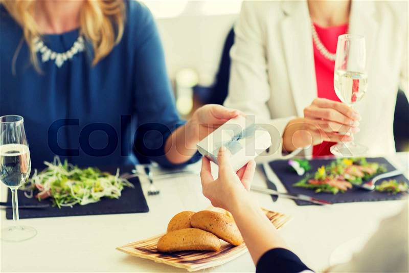People, holidays, celebration and lifestyle concept - close up of women giving birthday present at restaurant, stock photo