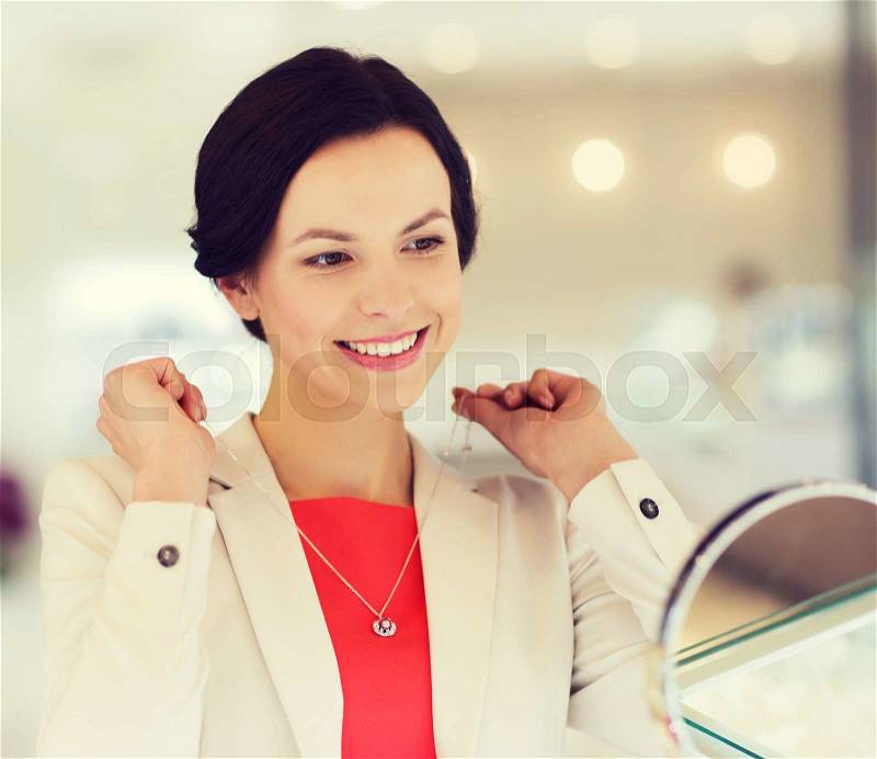 Sale, consumerism, shopping and people concept - happy woman choosing and trying on pendant at jewelry store, stock photo