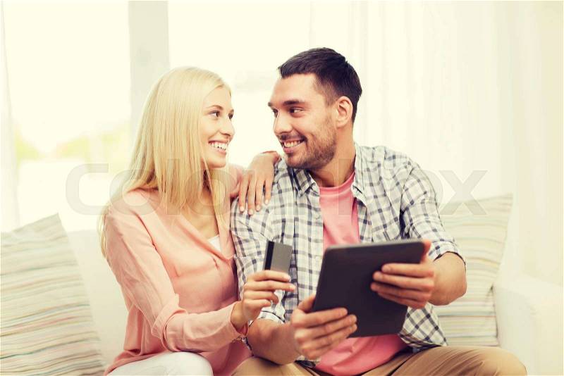 Technology, people, e-money and commerce concept - smiling happy couple with tablet pc computer and credit or bank card shopping online at home, stock photo