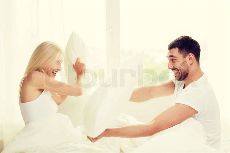 People, family, bedtime and fun concept - happy couple having pillow fight in bed at home, stock photo