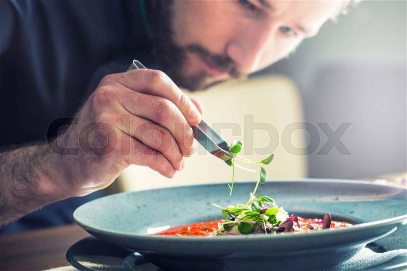 Chef in hotel or restaurant kitchen cooking, only hands. He is working on the micro herb decoration. Preparing tomato soup, stock photo