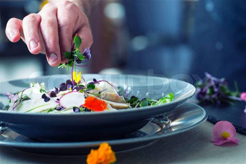 Chef in hotel or restaurant kitchen cooking, only hands. He is working on the micro herb decoration. Preparing vegetable salad with pieces of grilled chicken meat - virgin sirloin, stock photo