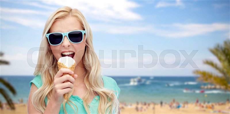 Summer holidays, travel, junk food and people concept - young woman or teenage girl in sunglasses eating ice cream over exotic tropical beach with palm trees and sea background, stock photo