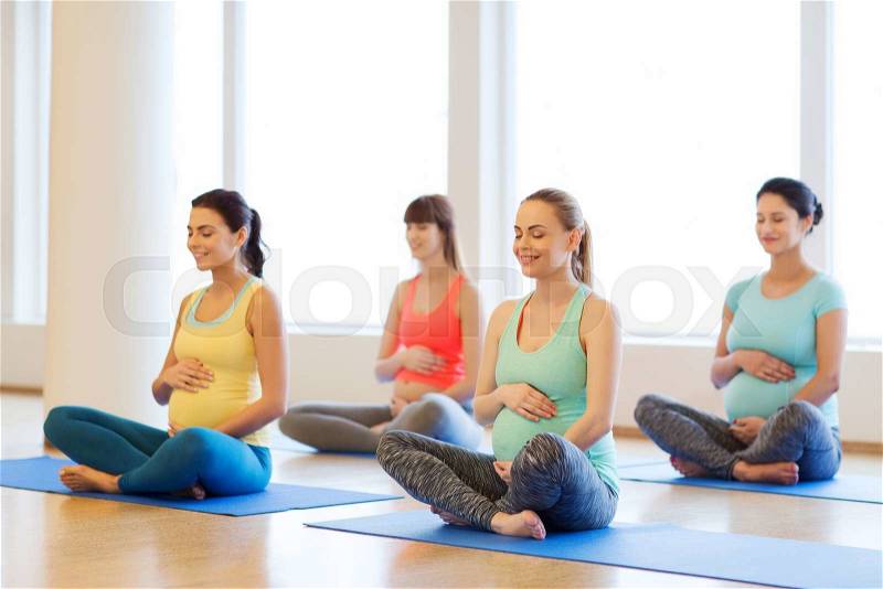 Pregnancy, sport, fitness, people and healthy lifestyle concept - group of happy pregnant women exercising yoga and and meditating in lotus pose in gym, stock photo