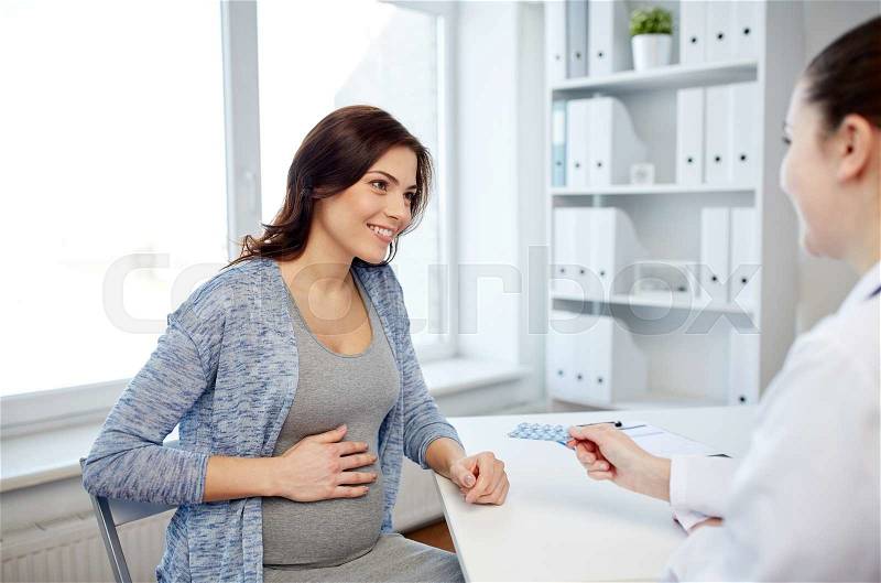Pregnancy, gynecology, medicine, health care and people concept - smiling gynecologist doctor giving pills to pregnant woman meeting at hospital, stock photo