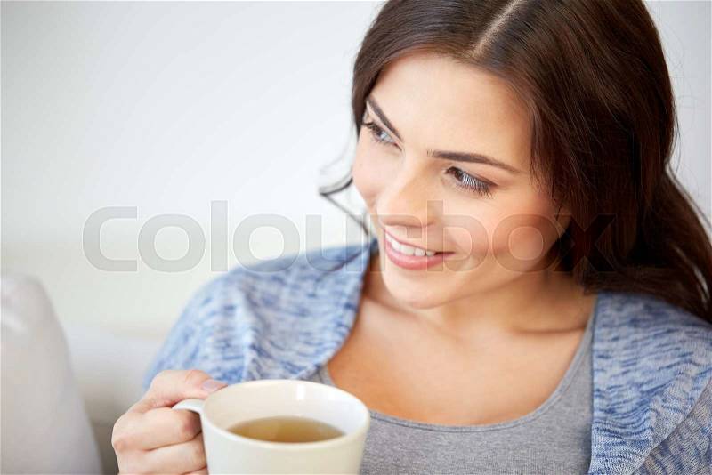 People, drinks and leisure concept - happy young woman with cup of tea at home, stock photo