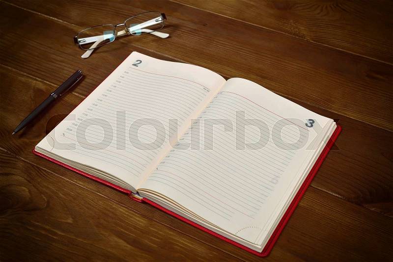 Open red leather diary, glasses and pen on wooden desk, stock photo
