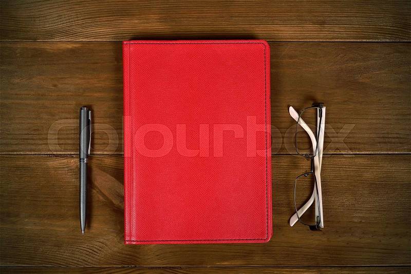 Top view blank red leather diary, glasses and pen on wooden desk, stock photo