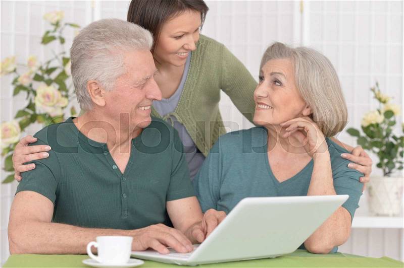 Senior couple portrait with laptop with caring daughter, stock photo