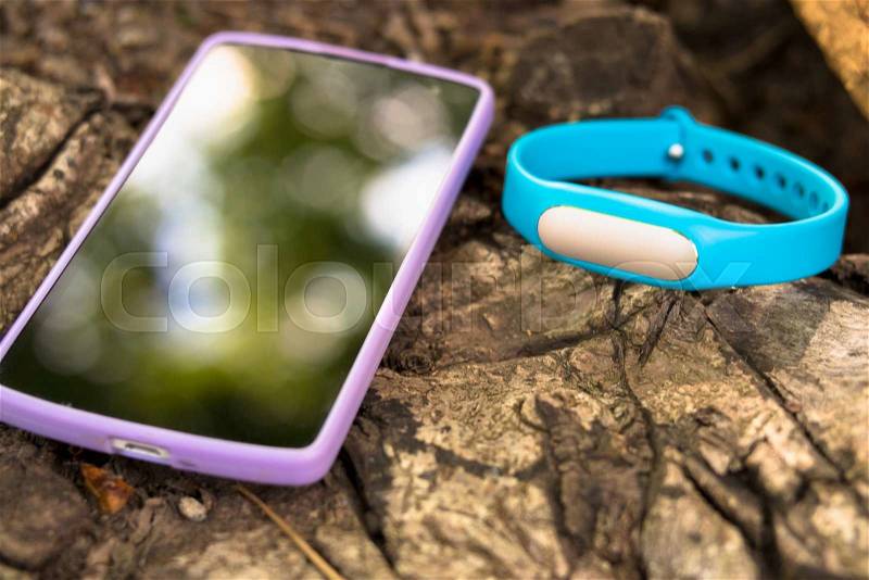 Fitness tracker and smart phone lying on a tree stump in the forest, stock photo