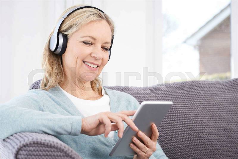 Mature Woman Streams Music From Digital Tablet To Wireless Headphones, stock photo