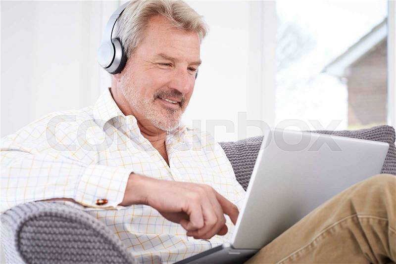 Mature Man Streams Music From Laptop To Wireless Headphones, stock photo