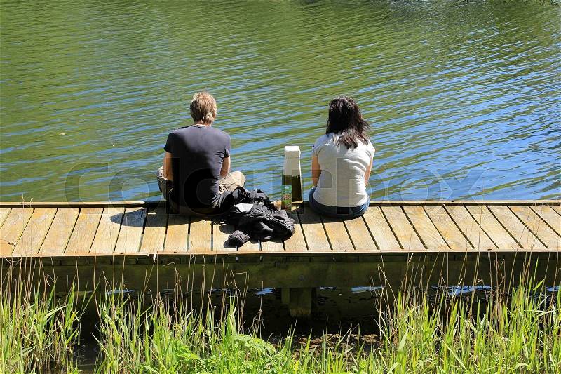 Couple, man and wife, sitting on the wharf and looking to the pond in the wonderful park in the summer, stock photo