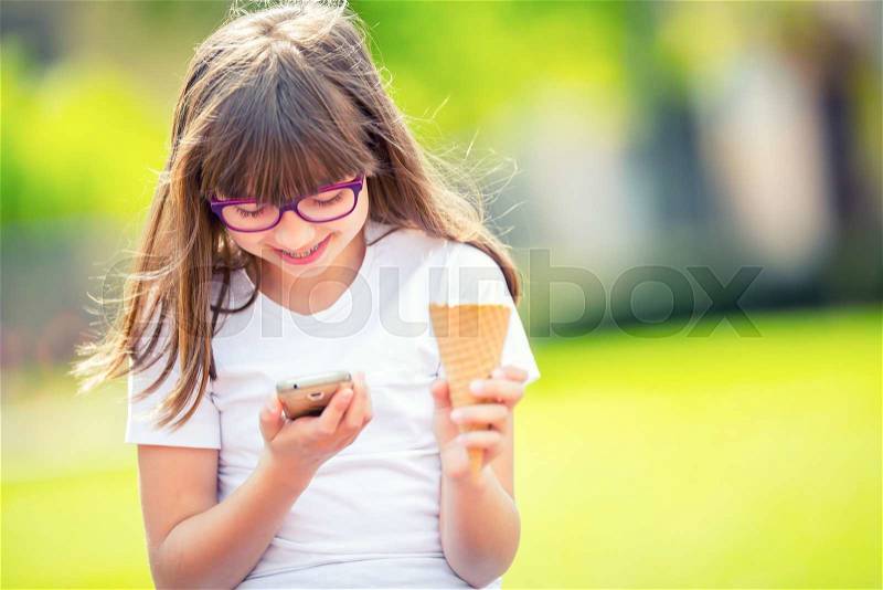 Cute little girl in the park on a sunny day with ice cream and mobile phone, stock photo