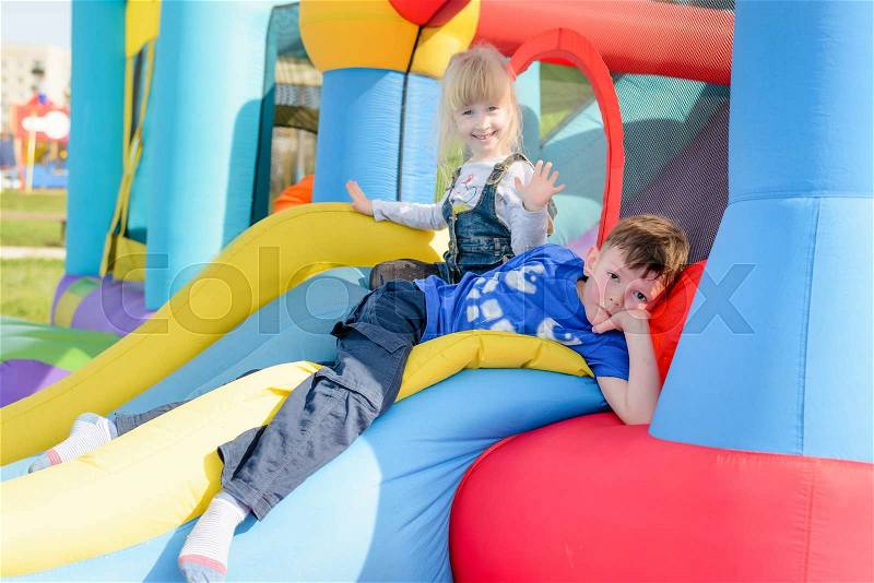 Cute young brother and sister having fun as they lay down on inflatable blue, yellow and red castle and slide, stock photo